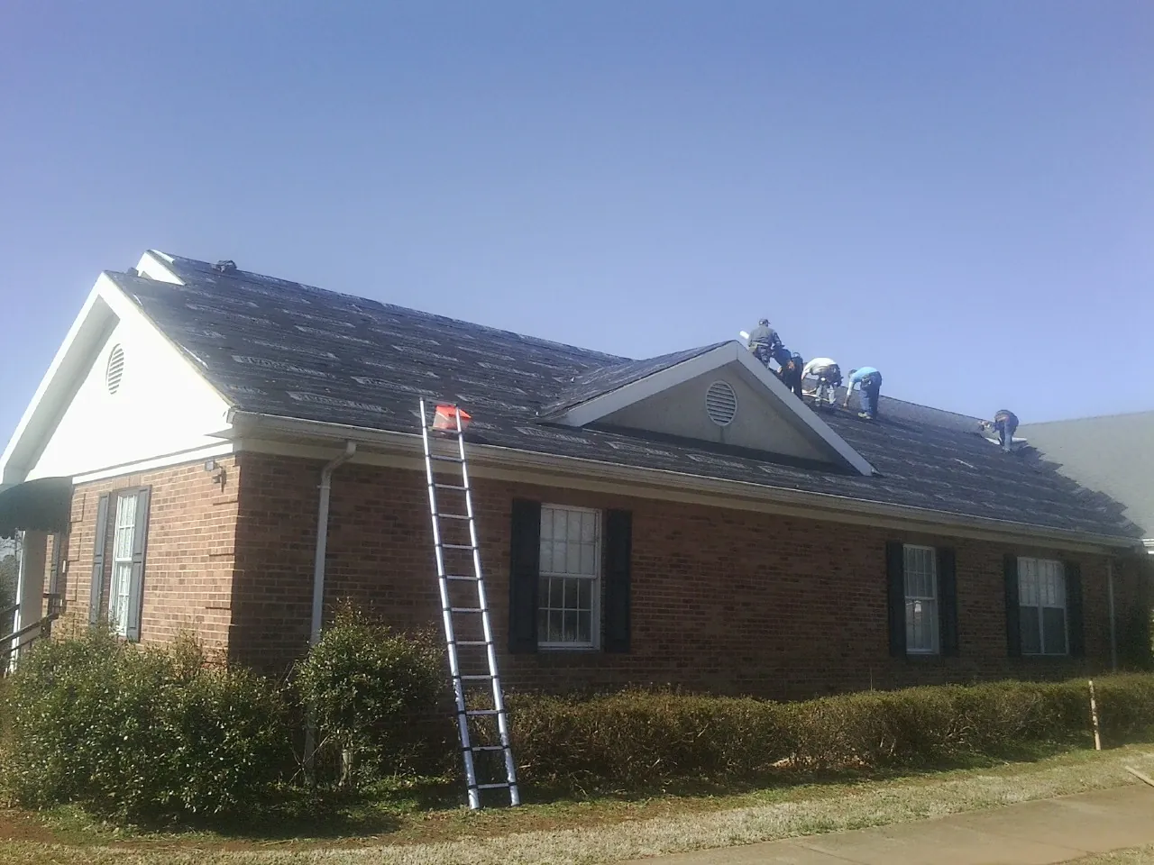 Crew tearing shingles off a brick ranch roof with a ladder set — Metal Roof Repair work by our crew in Chico